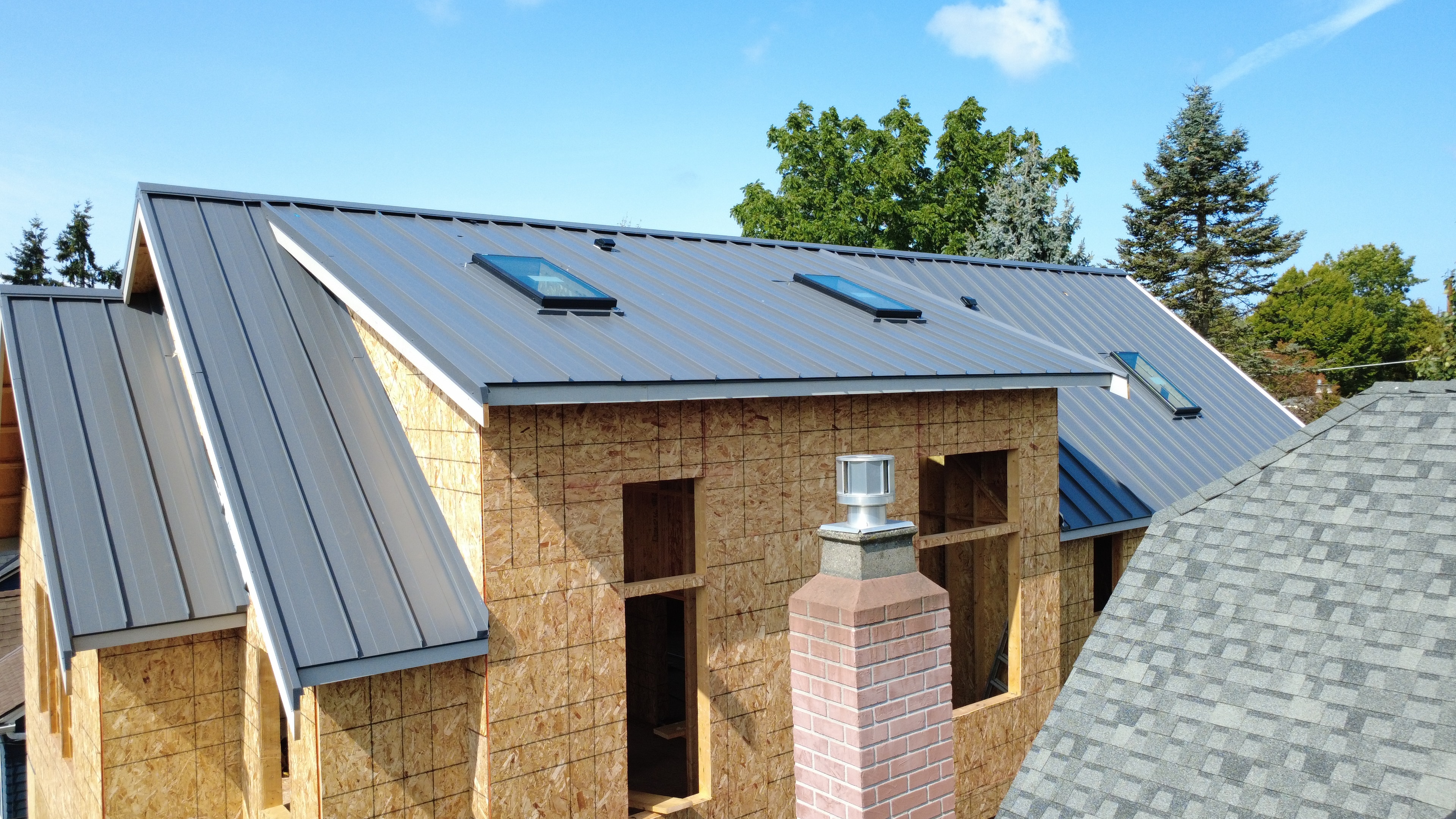 Aerial view of standing seam metal roof with skylights and brick chimney on residential home