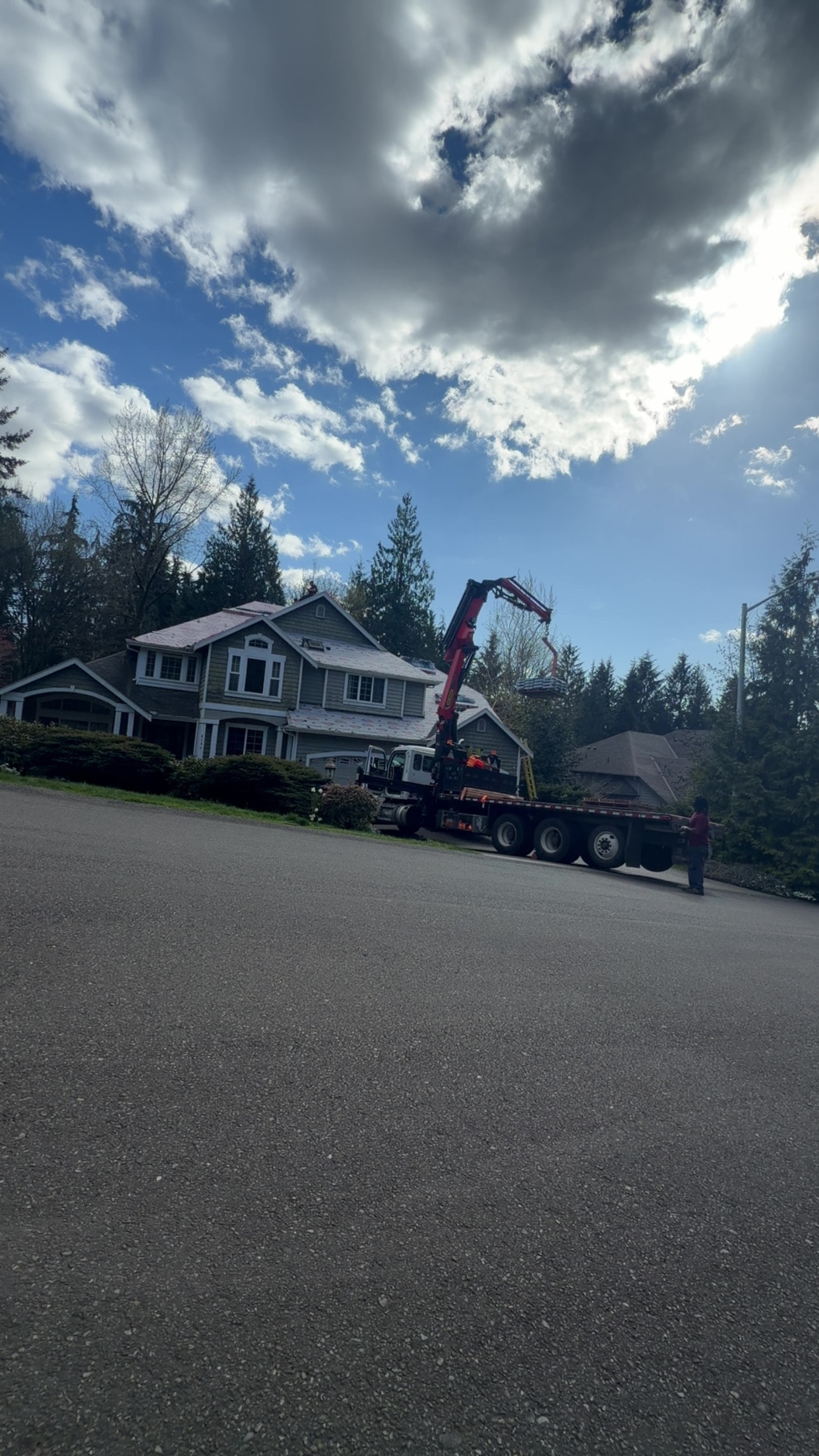 Crane truck delivering roofing materials to a large residential home during a roof replacement project