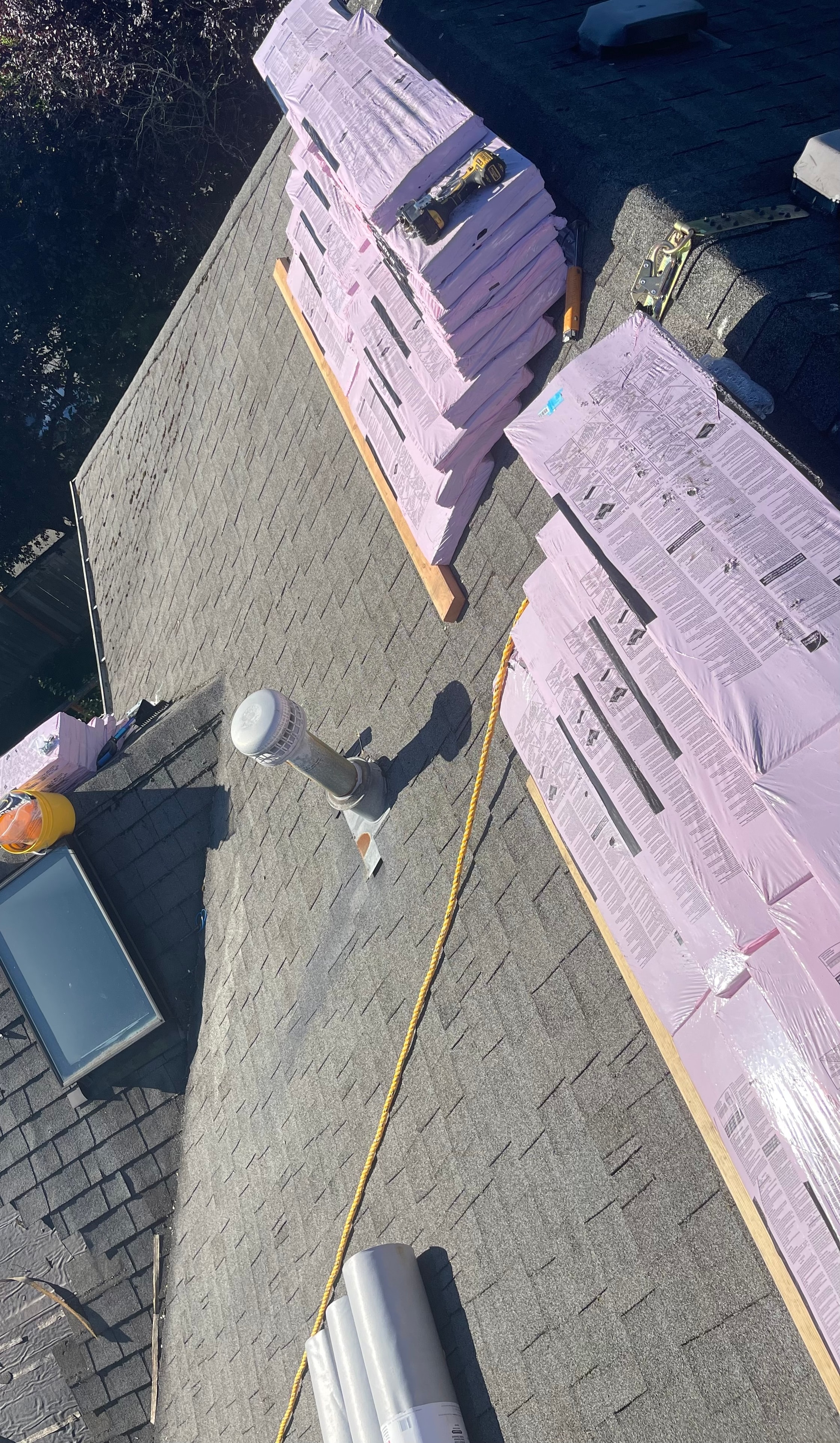 Aerial view of residential roof with shingle bundles and safety rope visible during active installation