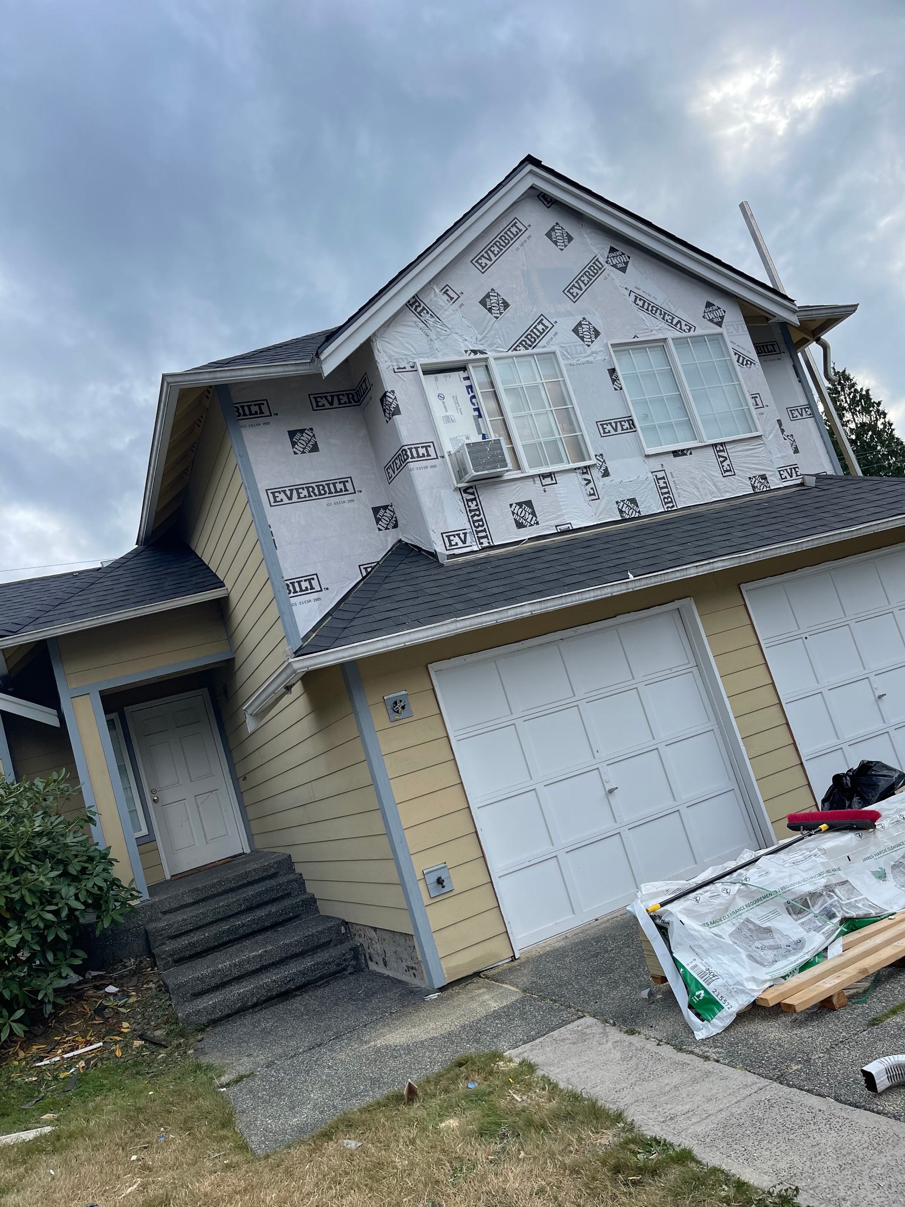 Two-story residential home with Everbilt weather barrier installed on upper siding and completed dark shingle roof below